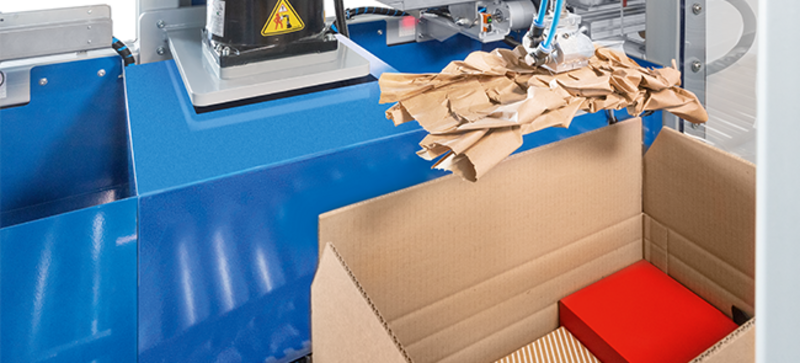 A paper cushion is placed fully automatically in a box containing goods for shipment.