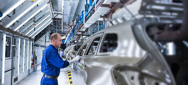 Ein Mann arbeitet an einem Auto in einer Produktionshalle